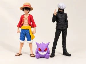 Pack Otaku — composition complète Figurines Luffy et Gojo avec un étui AirPods Pro Gengar violet sur fond ivoire.